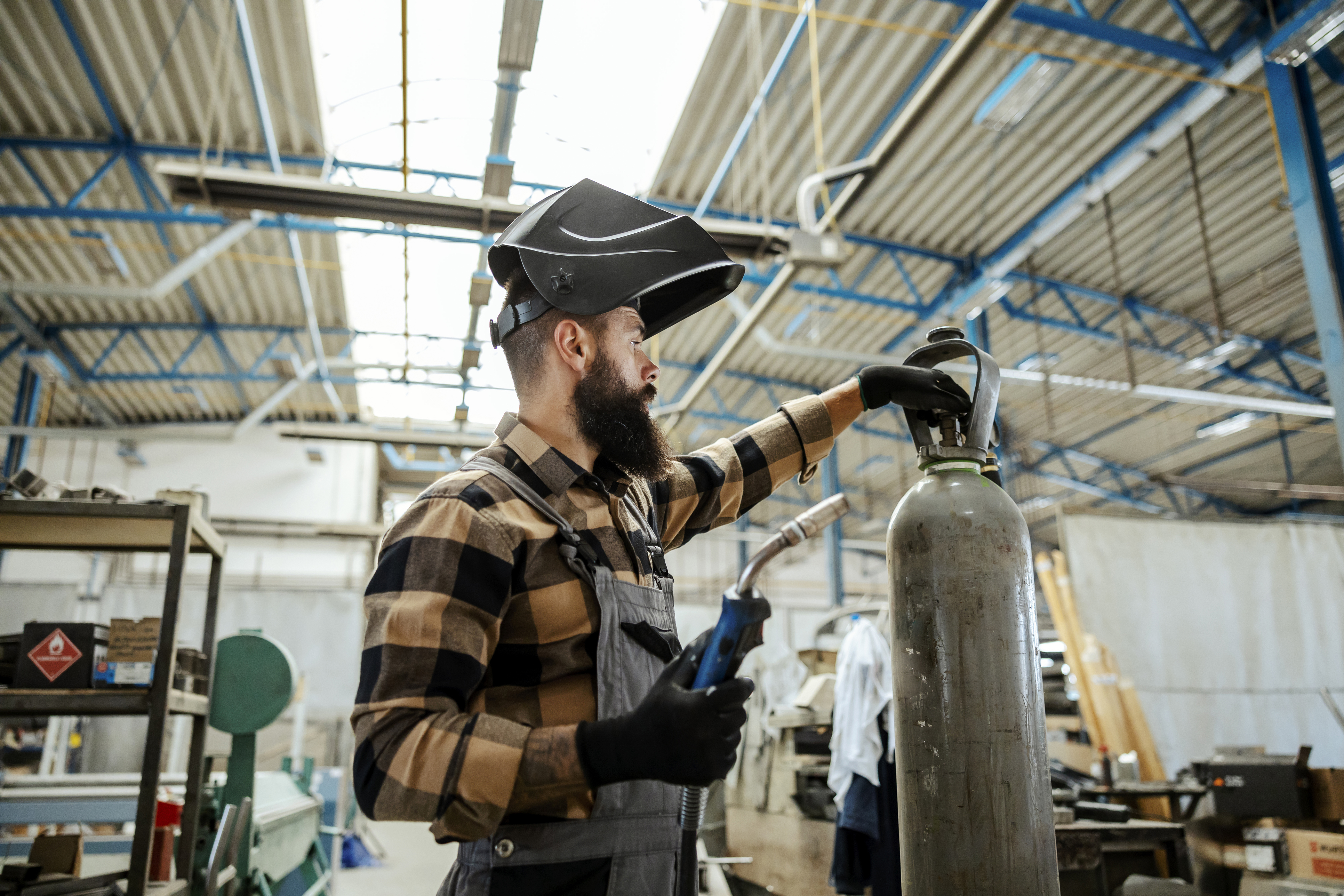 A worker with a protective mask on his head unscrews the valve on the gas bottle and prepares for welding